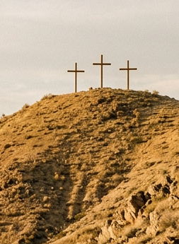 Three crosses on a desert hill overlooking mountains and a winding road